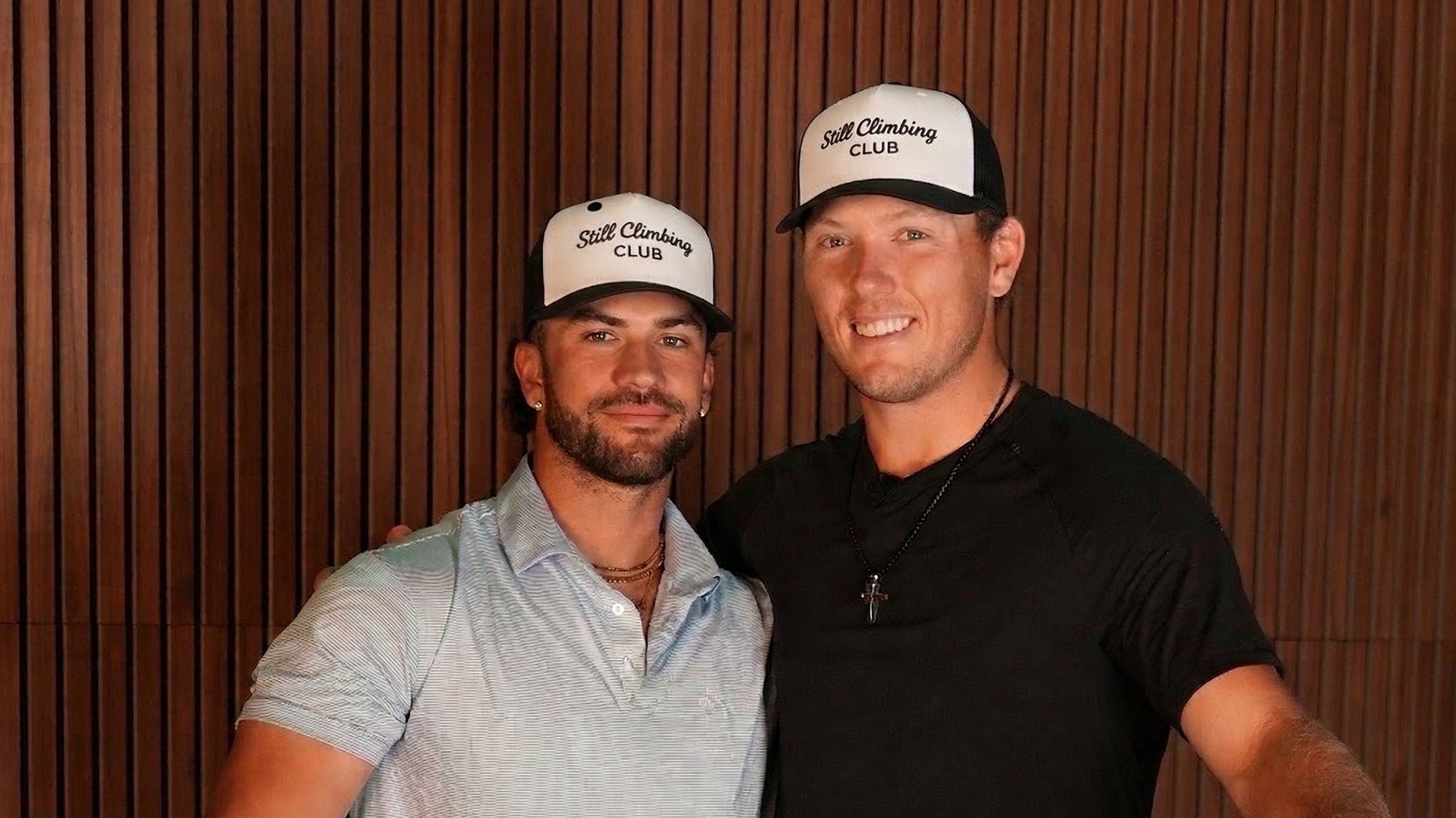 Two men wearing 'Stiill Clubbing Club' hats against a wooden paneled wall.