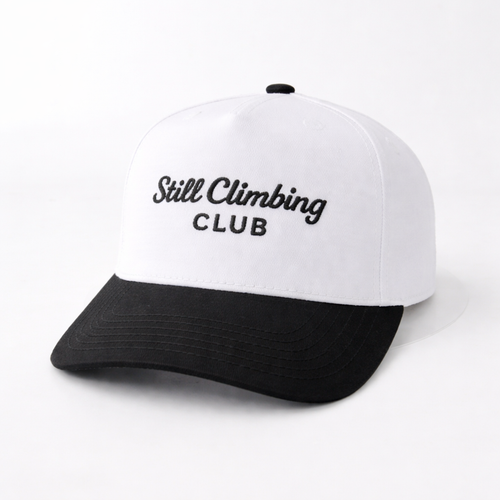 White and black cap with 'Still Climbing Club' text on a white background